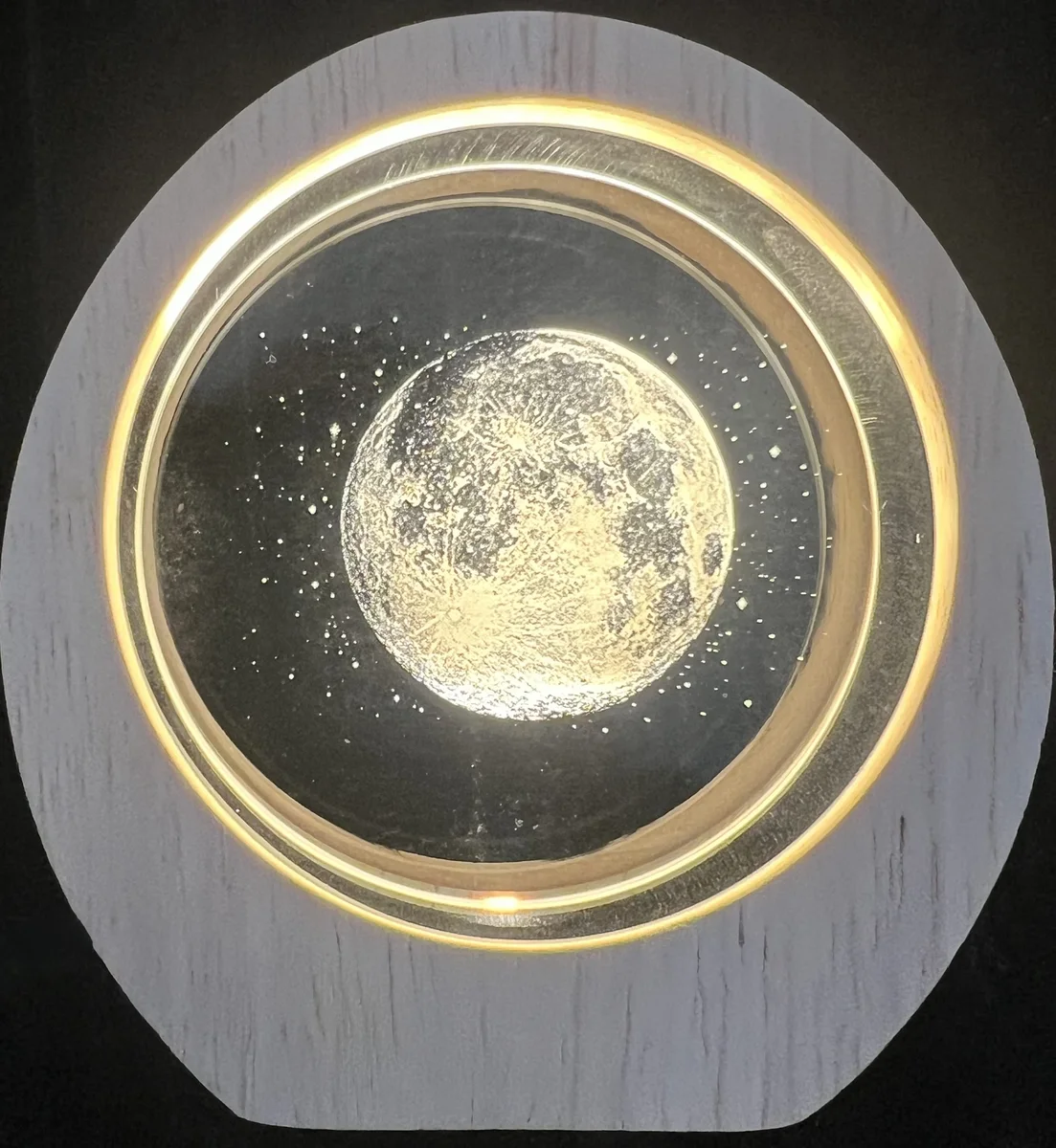 Crystal bedside lamp — round crystal disc with the moon and stars engraved inside, standing on its white-washed wooden base with a warm LED ring